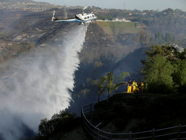 Firefighters look on as a helicopter drops water