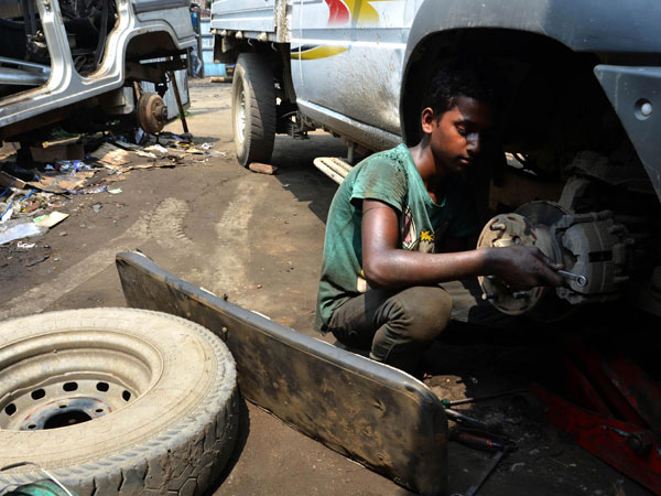 A boy works on a car at a vehicle repair garage