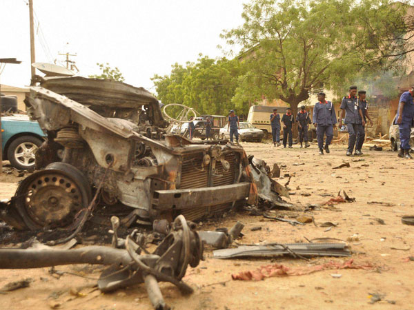 People walk past the remains of a car used for a suicide bomb