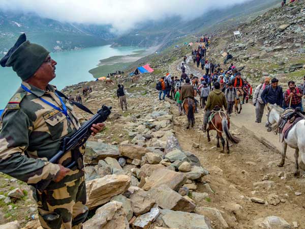 Security personnel look on as a batch of pilgrims are on their way towards the holy cave shrine of Amarnath near Sheshnag Lake