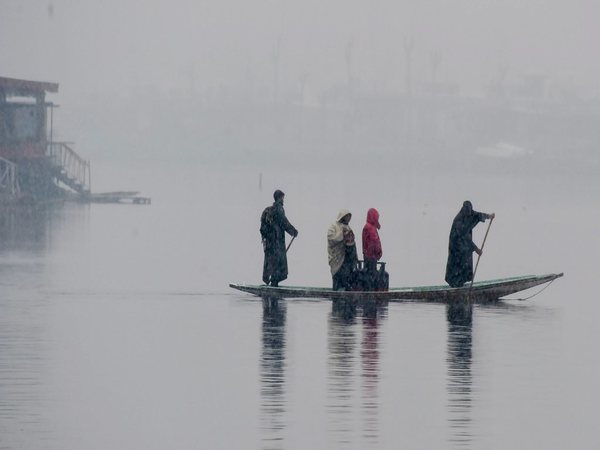 Boatmen row a boat during fresh snowfall at Dal Lake in Srinagar